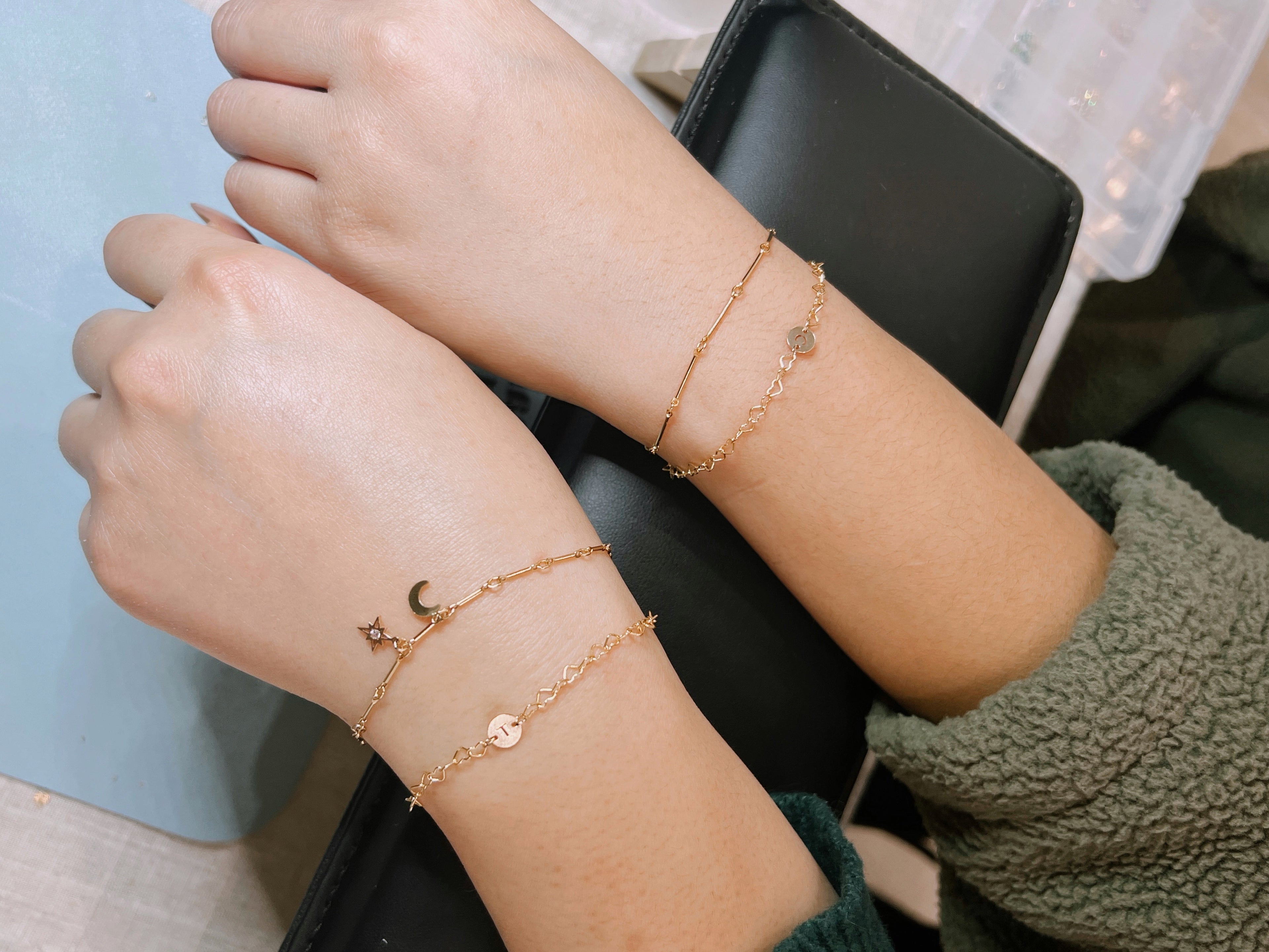 Two wrists wearing gold anklets with star and moon designs on a neutral background.